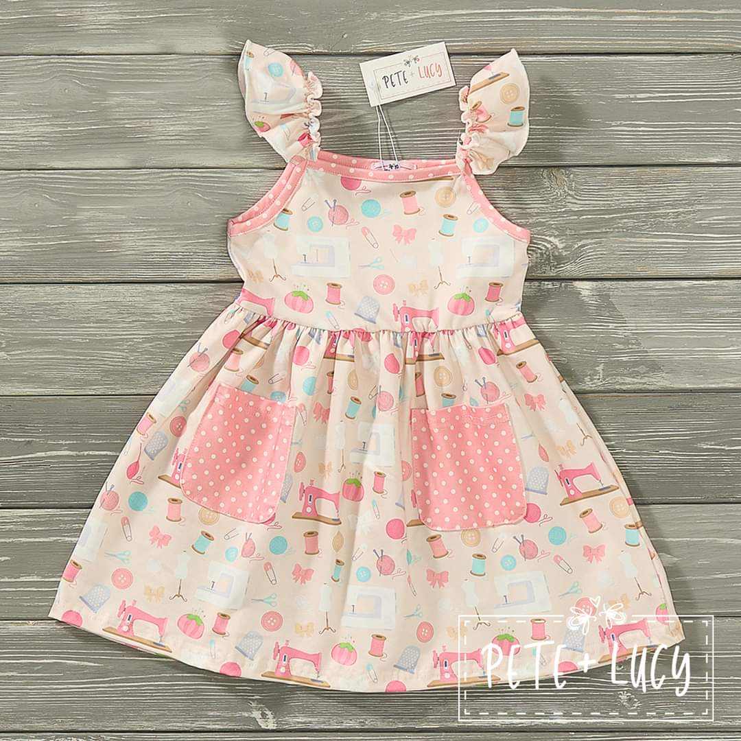 Pink Sewing Kit Dress with playful patterns, ruffled straps, and polka dot pockets.