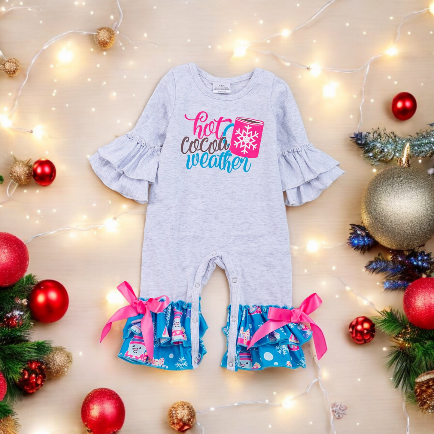 Baby romper with Hot Cocoa Weather print, flutter sleeves, and ruffle pant bottoms with pink bows, perfect for winter.