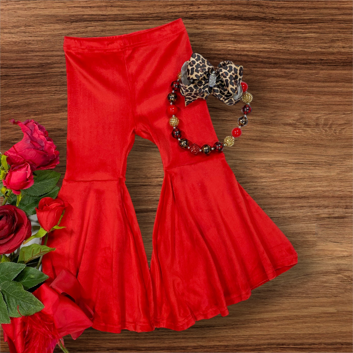 Red velvet bell bottom pants with wide legs on wooden background with floral and beaded accessories