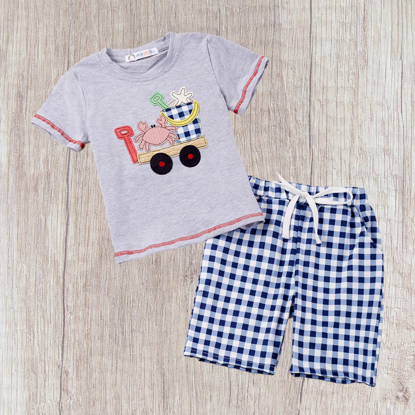 Boy's sand adventure outfit with a playful beach-themed gray top and blue checkered shorts.
