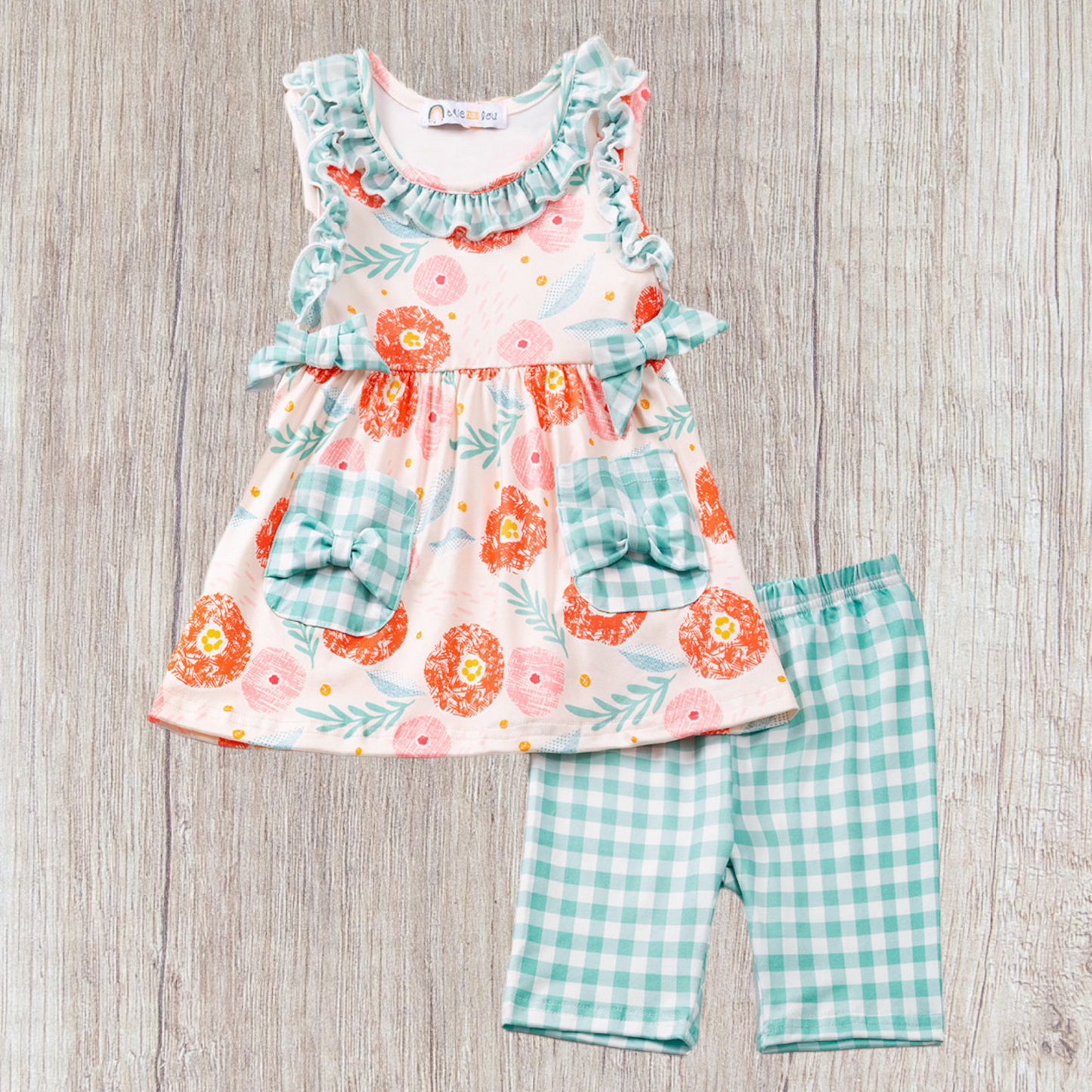 Jeannie 2 Piece Outfit featuring floral top and checked shorts on wooden background.