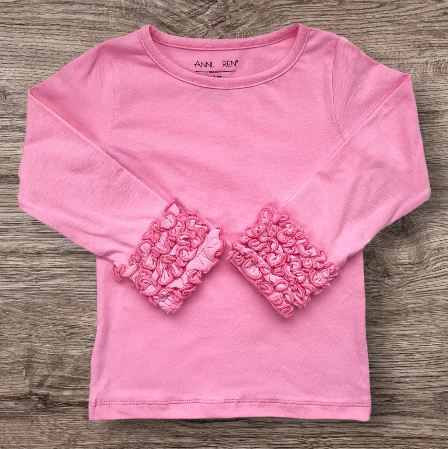 Pink long sleeve ruffle shirt for girls on wooden surface.