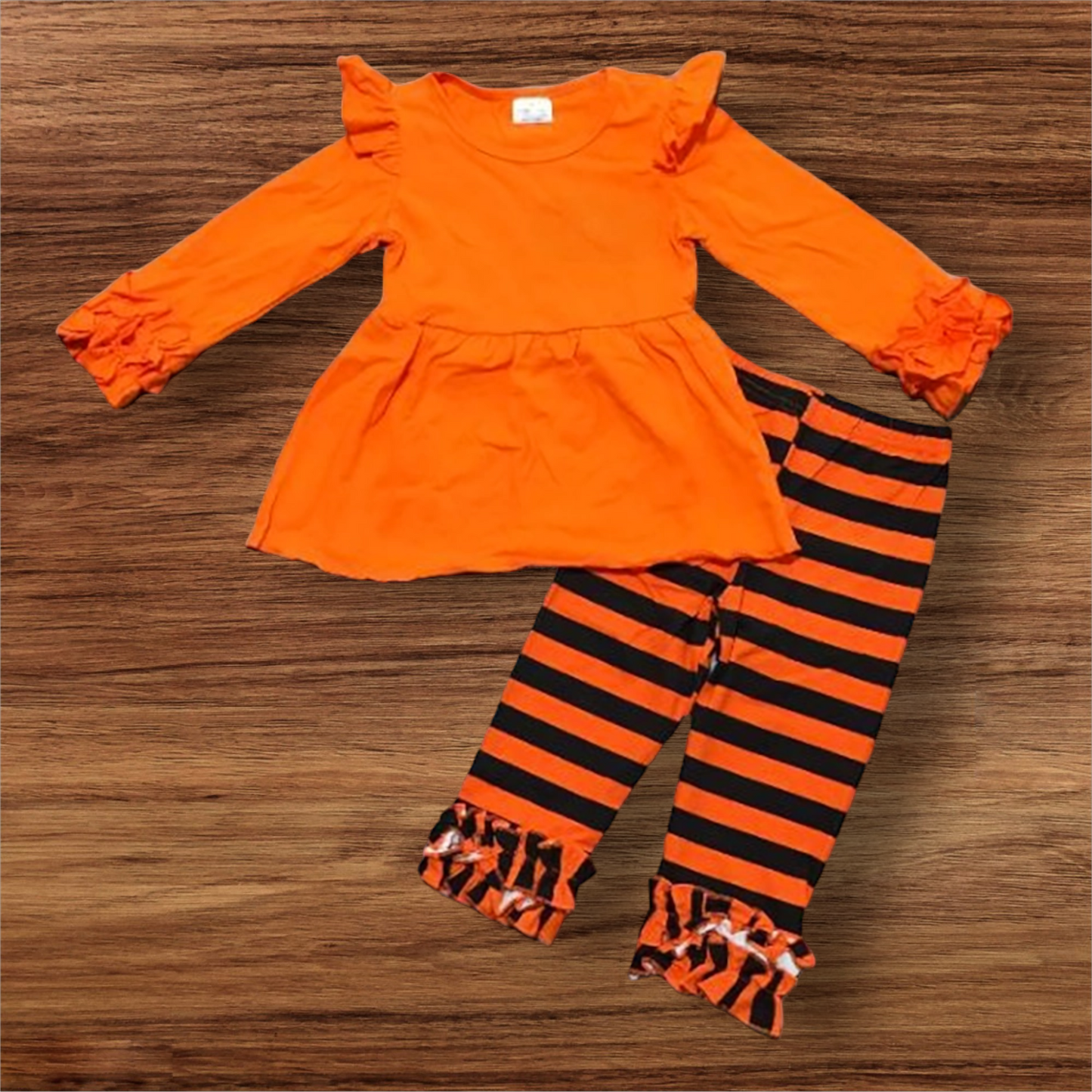 Bright orange pumpkin patch perfection outfit with long ruffled sleeves and black striped leggings.