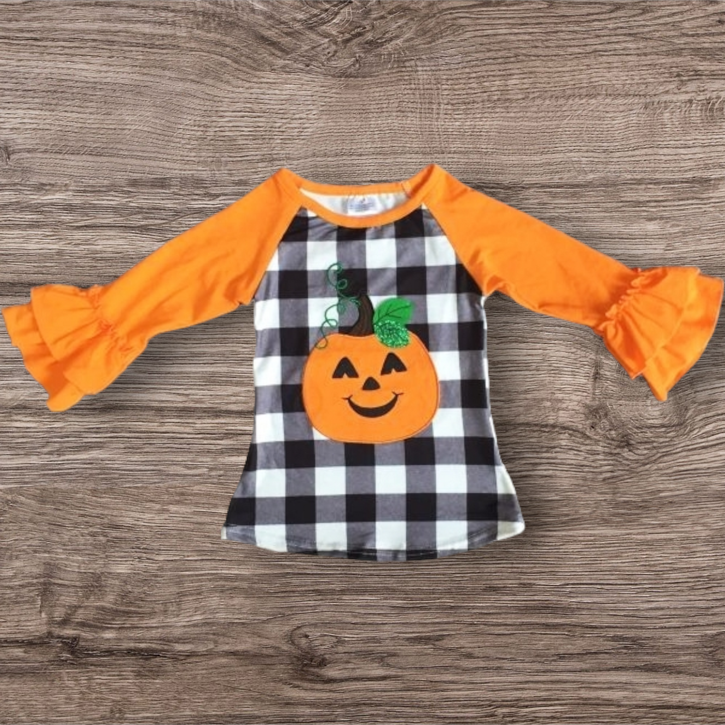 Fall Pumpkin Ruffle Shirt with jack o lantern applique and orange ruffled long sleeves on black and white checkered background