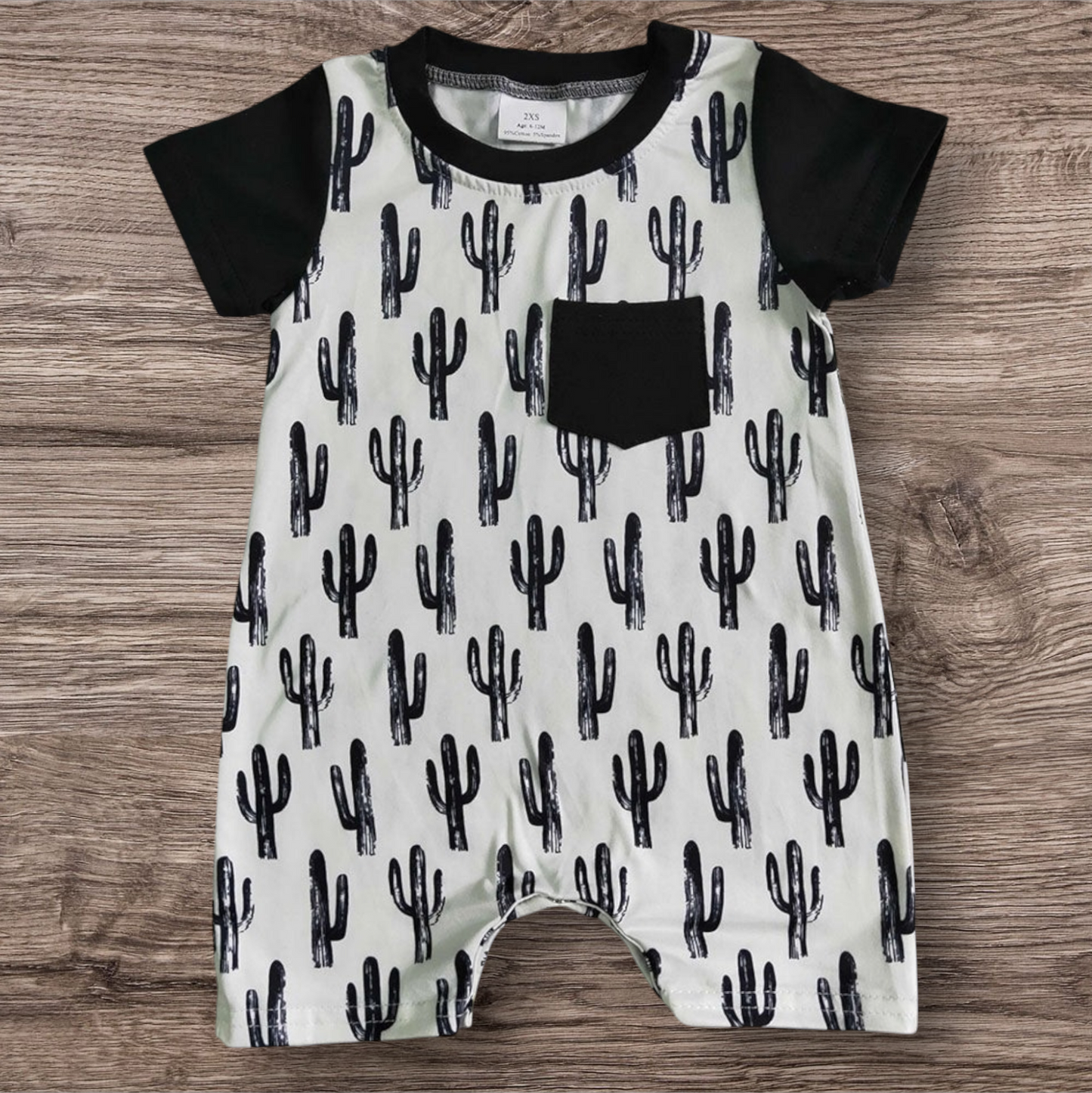 Black Cactus Romper with short sleeves and cactus print on wooden background.