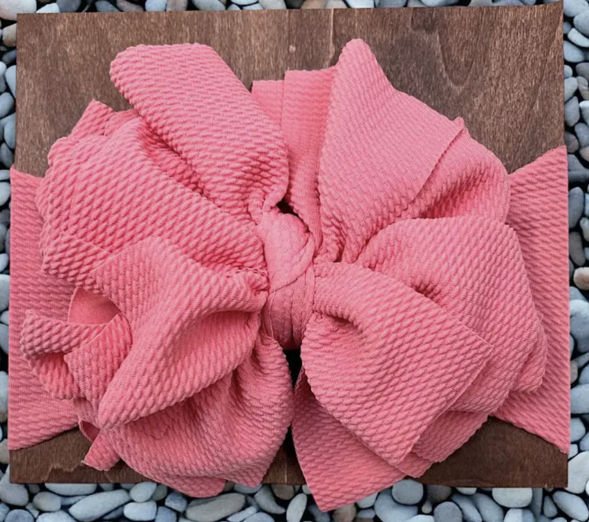 Jumbo pink textured bow accessory on wooden background.