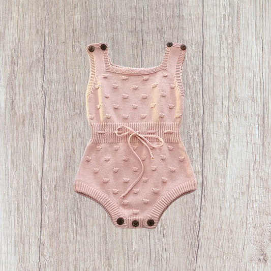 Knitted pink baby bodysuit with polka dot pattern and bow tie waist, 100% cotton.