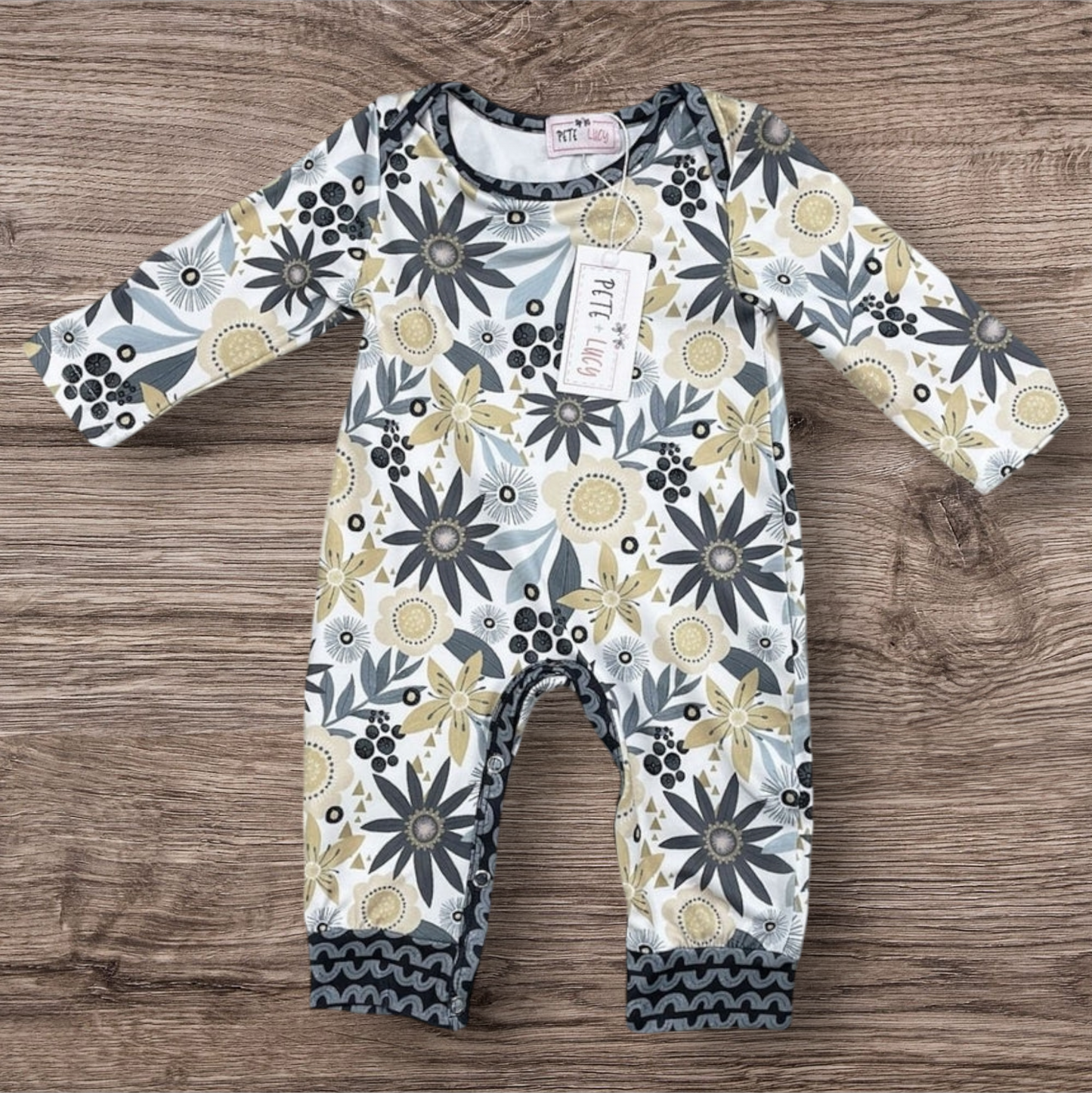 Golden Garden Romper with floral design on a wooden background.