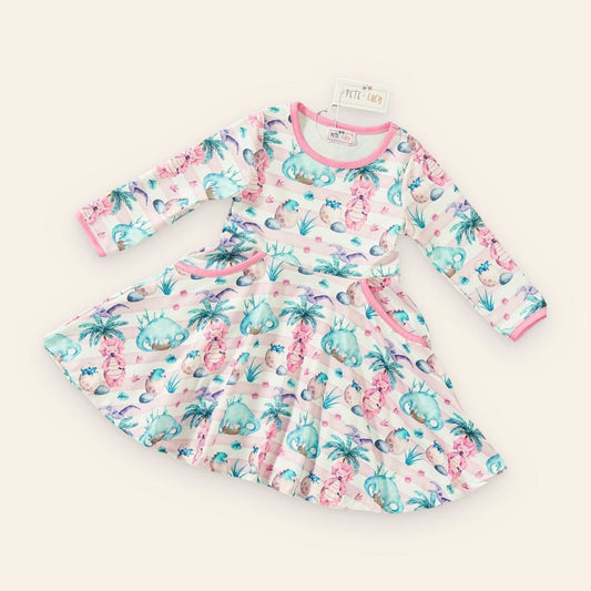 Mia Dinosaur Dress with playful dinosaur and palm tree print, long sleeves, and pockets.