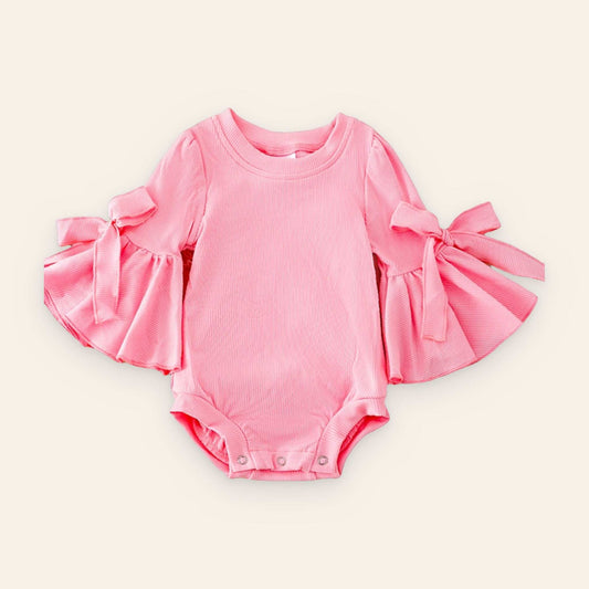 Pink bell sleeve baby onesie with snap closures on wooden background
