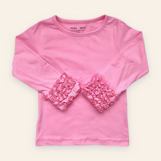 Pink long sleeve ruffle shirt for girls on wooden surface.